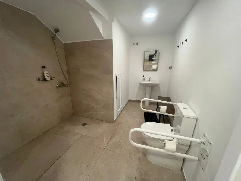 Baño accesible con ducha a ras de suelo, inodoro con barras de apoyo y lavabo
