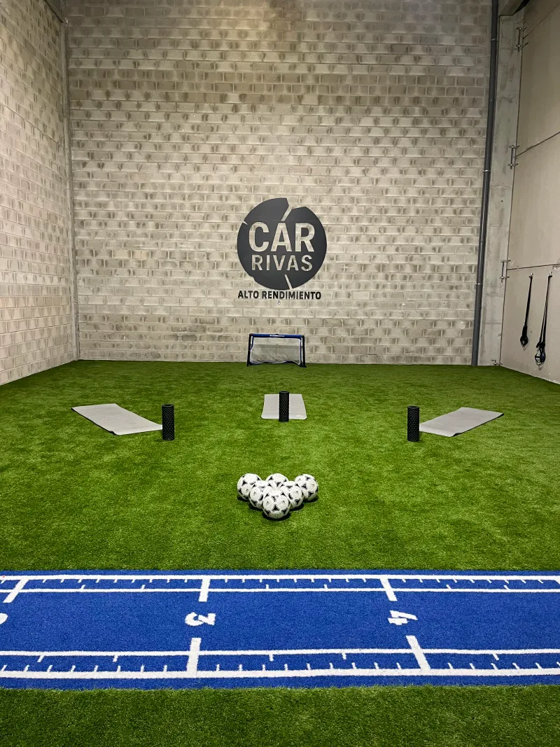 Pista de césped artificial interior con marcajes de medición y balones de fútbol